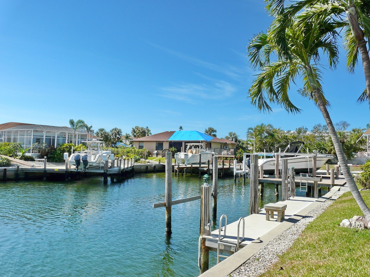 A marina with boats docked, a covered boat house, and a residential building with a blue roof.