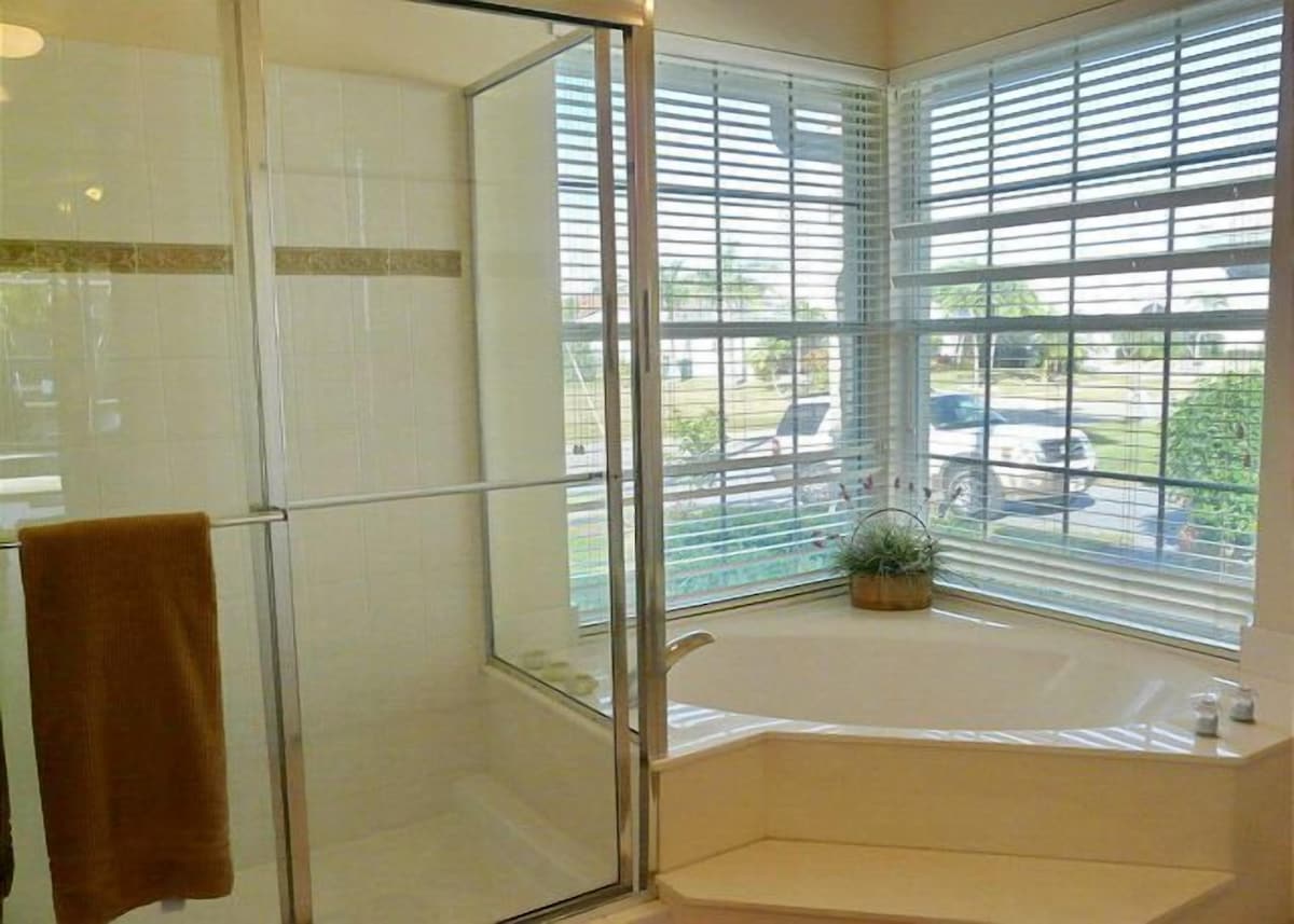 A modern bathroom with a glass shower enclosure, a bathtub, and a window with blinds.