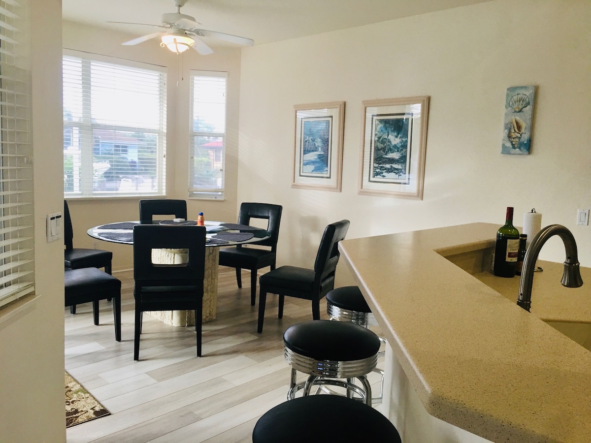 A dining area with a round table and chairs, a kitchen with a sink and countertop, and two framed pictures on the wall.