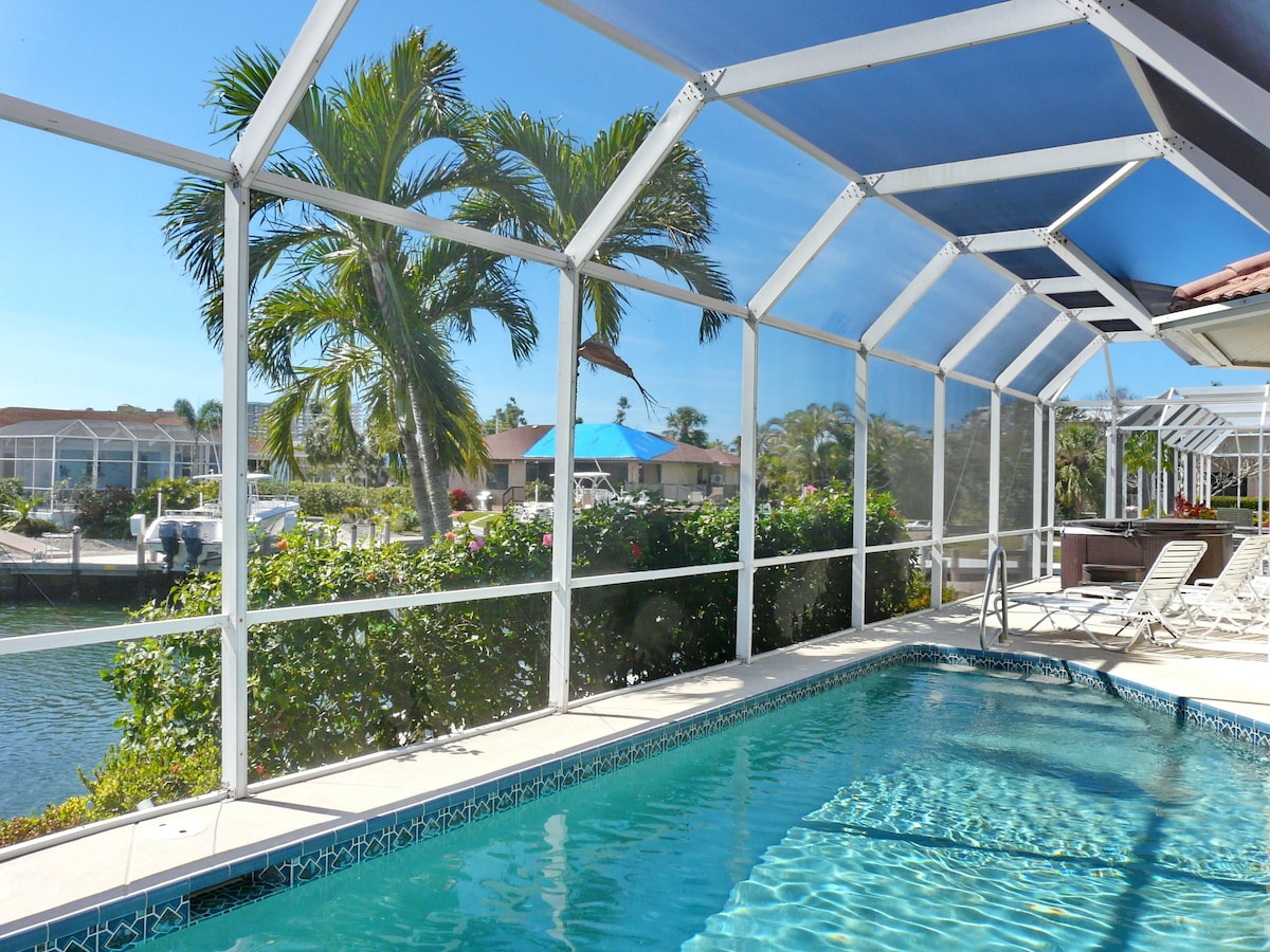 A pool area with a clear view of the water, a covered seating area, and surrounding greenery.