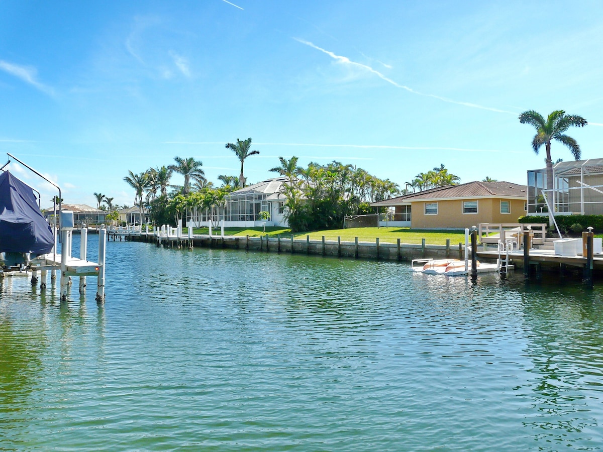 A marina with docked boats, a covered boat launch, and residential buildings with a clear sky.