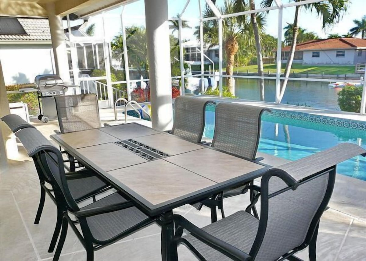 A covered outdoor seating area with a pool view, a grill, and a view of a residential area.
