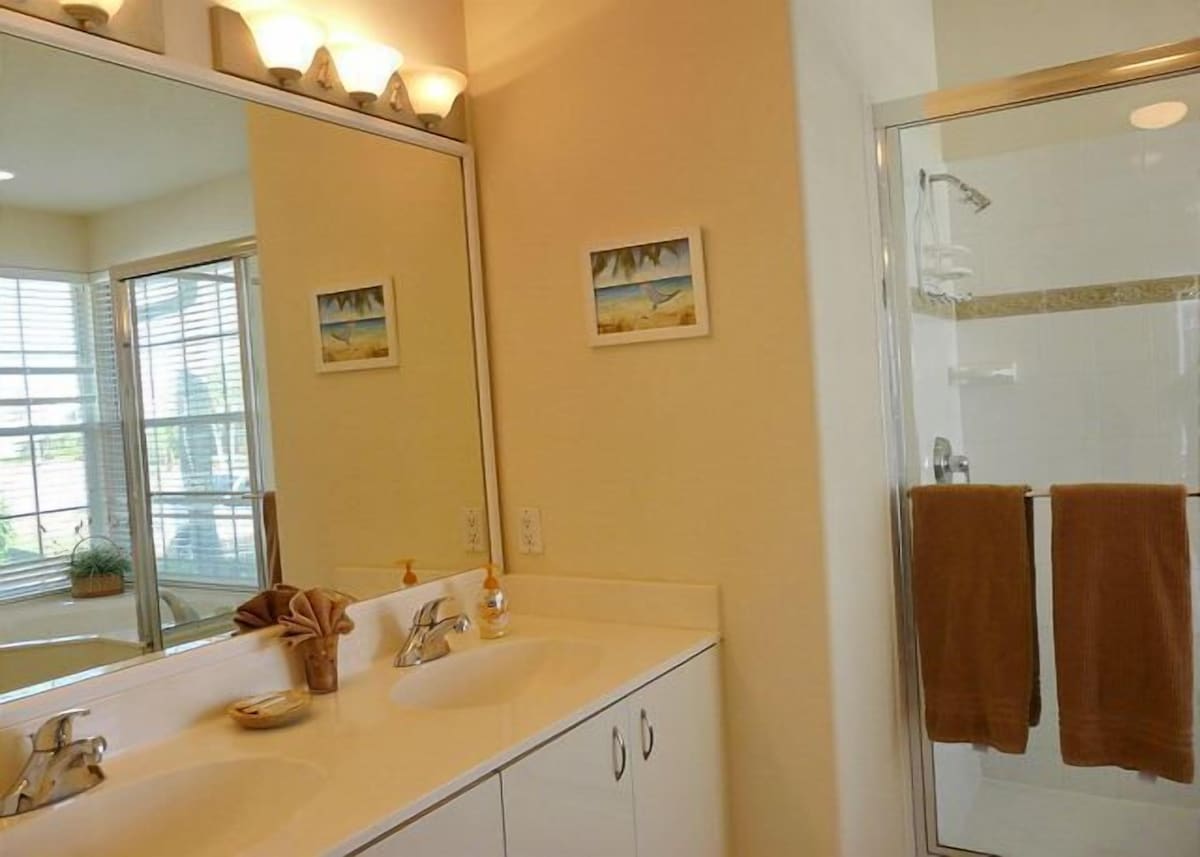 A bathroom with a large mirror, a sink, a shower, and two towels hanging on the wall.