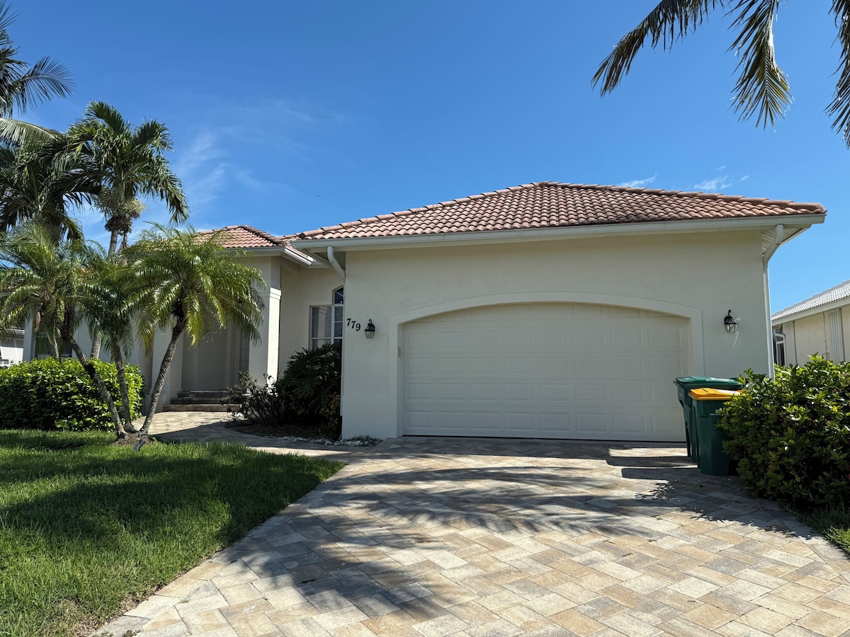 A residential house with a tiled roof, a garage, and a well-maintained lawn with palm trees.