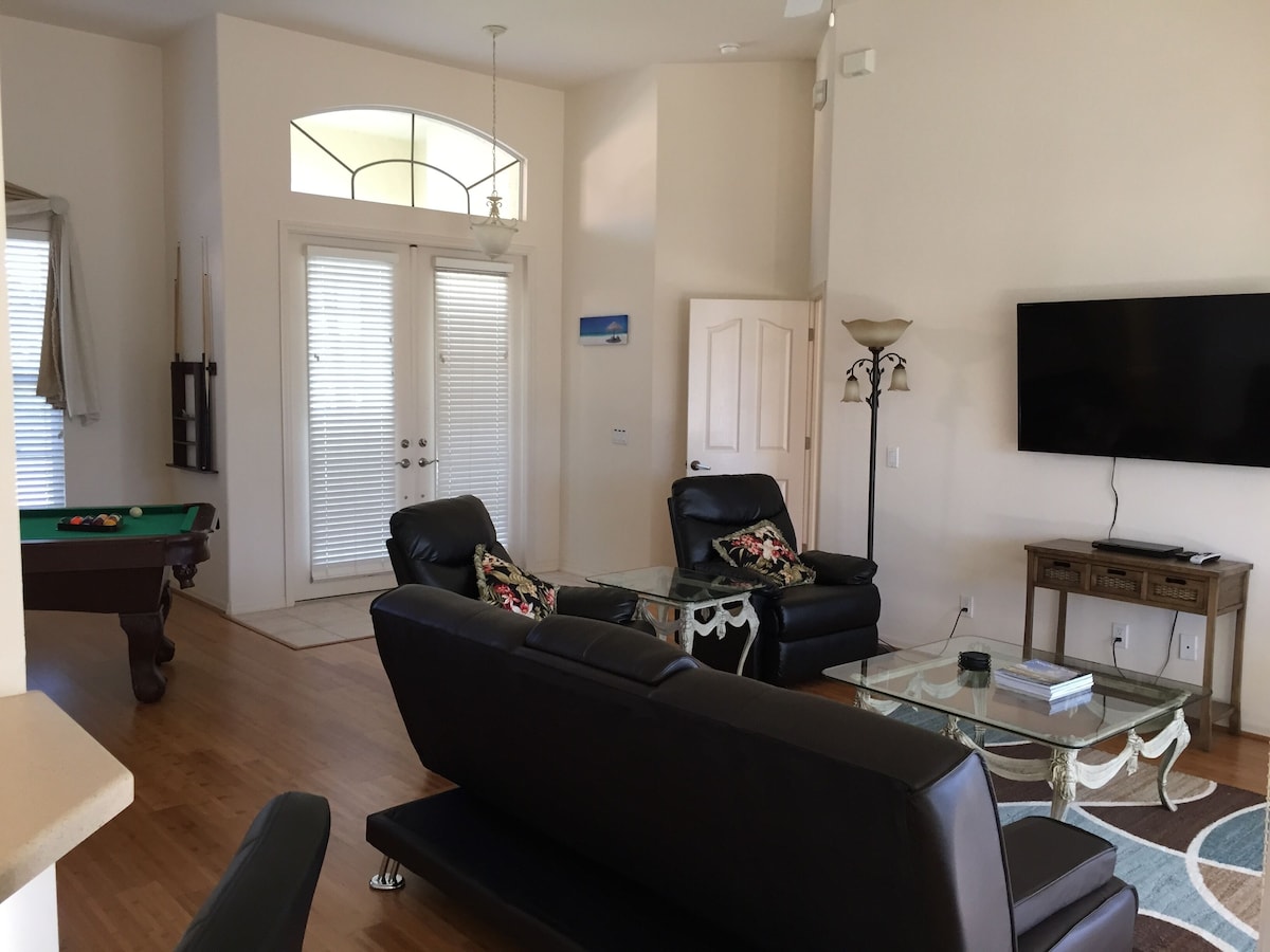 A living room with a pool table, two black leather sofas, a glass coffee table, a television, and a lamp.