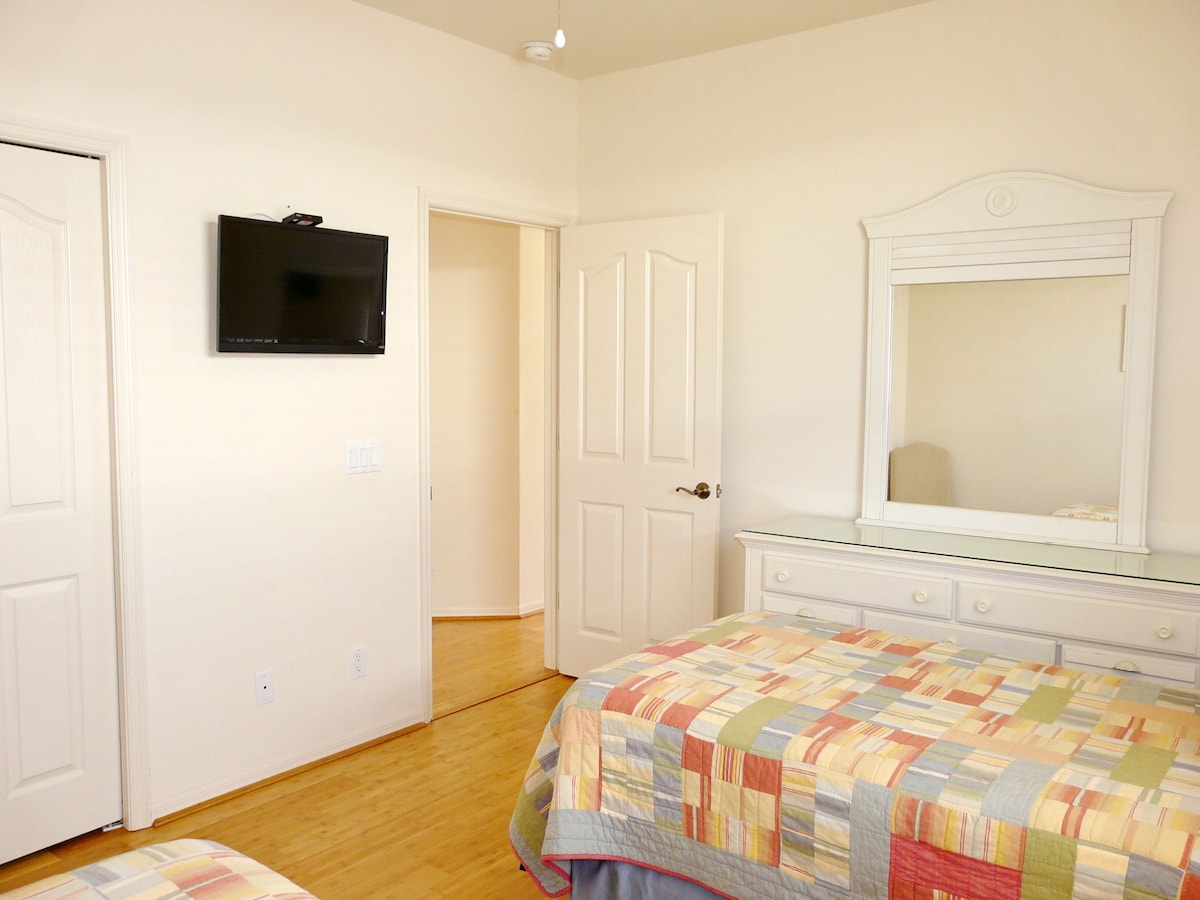 A bedroom with a bed, dresser, and a TV mounted on the wall.