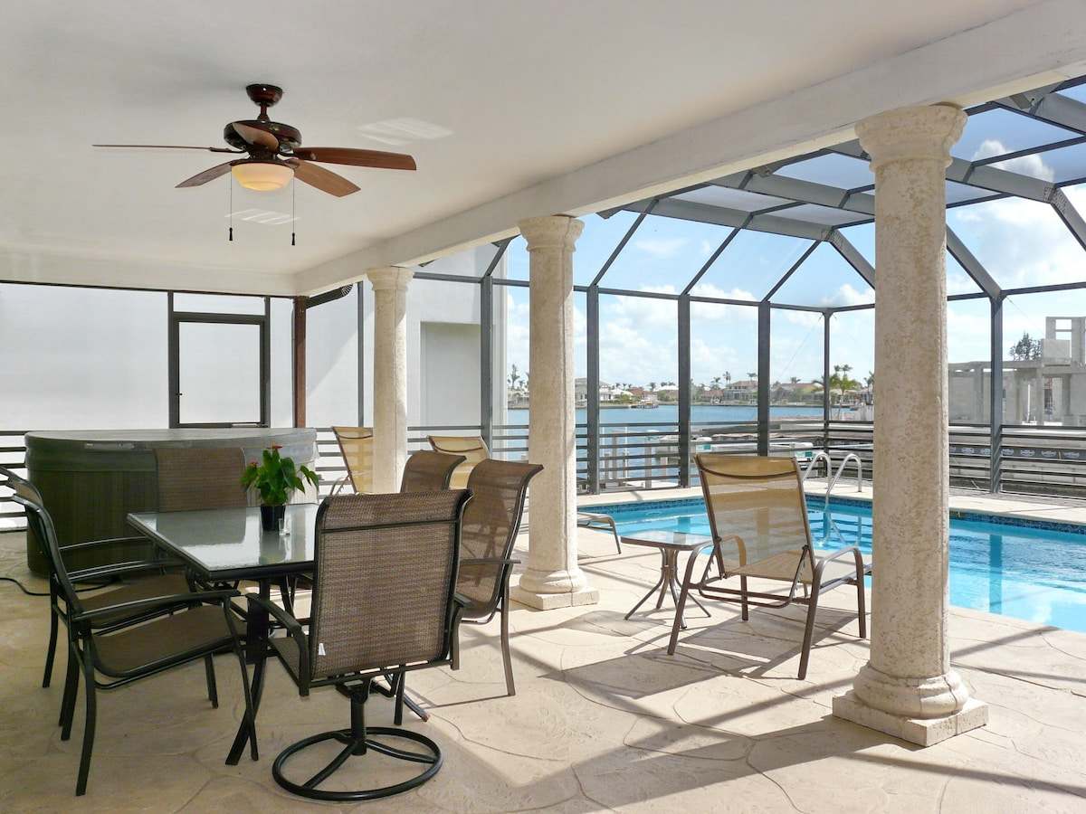 Lanai dining table beside a covered spa, with the pool and water view