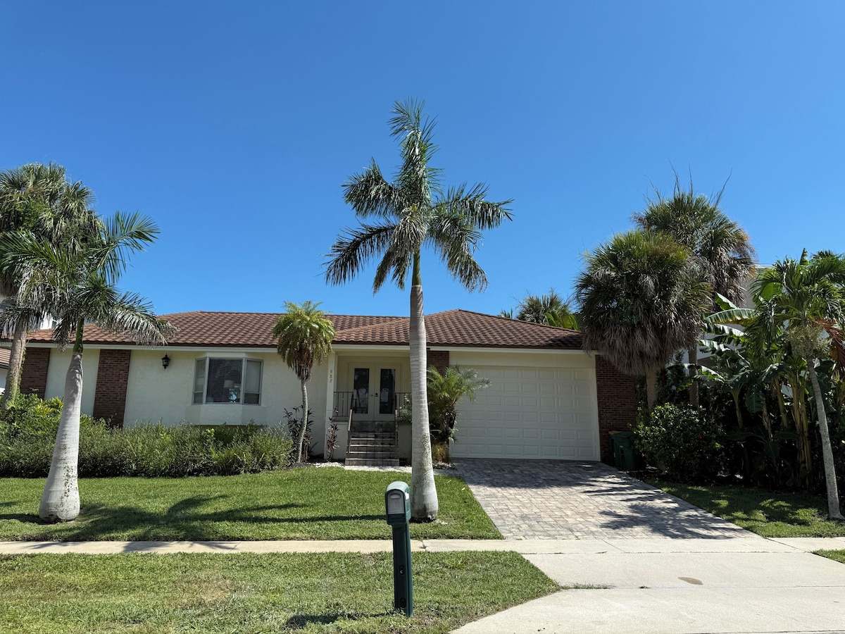 Front of the house with palms, a lawn, and a driveway