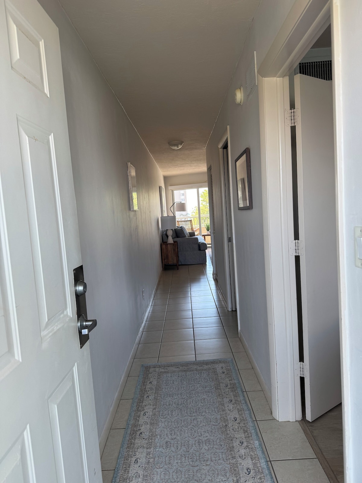 A hallway with white doors, a patterned rug, and a view into a living area with a sofa and a table.
