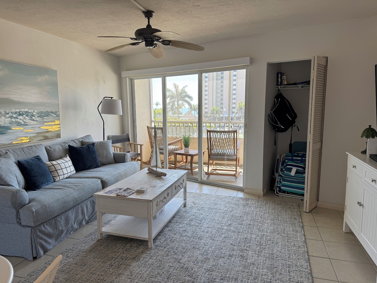 A living room with a sofa, coffee table, and a view of a balcony with outdoor furniture.