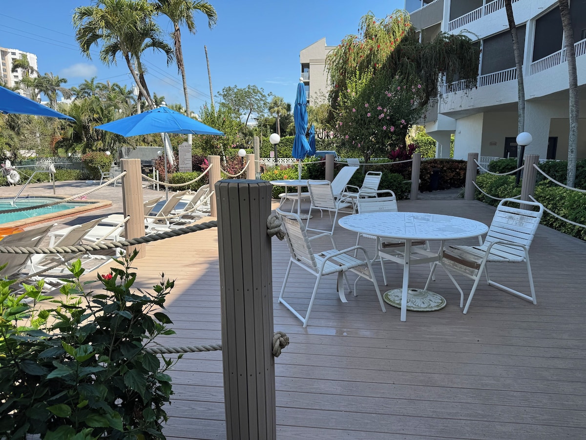 A poolside area with lounge chairs, a table, and umbrellas.