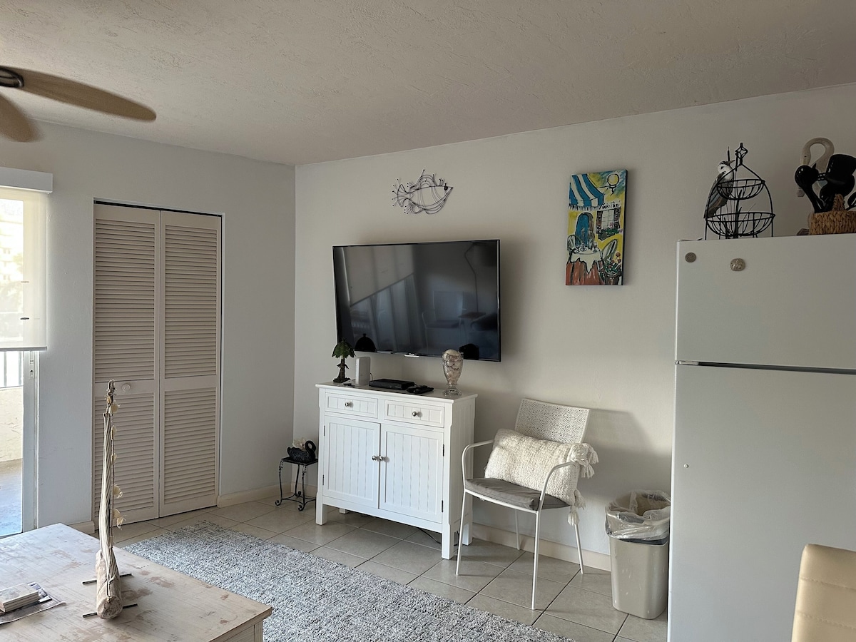 A living room with a television, a white cabinet, a chair, a small table, and a ceiling fan.