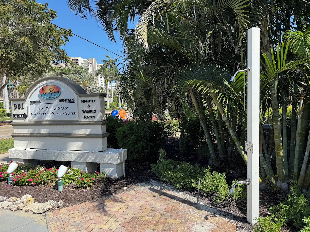 A sign for Marco Beach Vacation Suites with a beach club, office, and weekly rates.