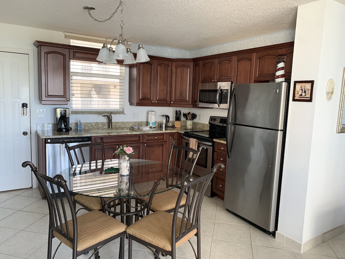 A modern kitchen with wooden cabinets, stainless steel appliances, and a glass dining table with chairs.