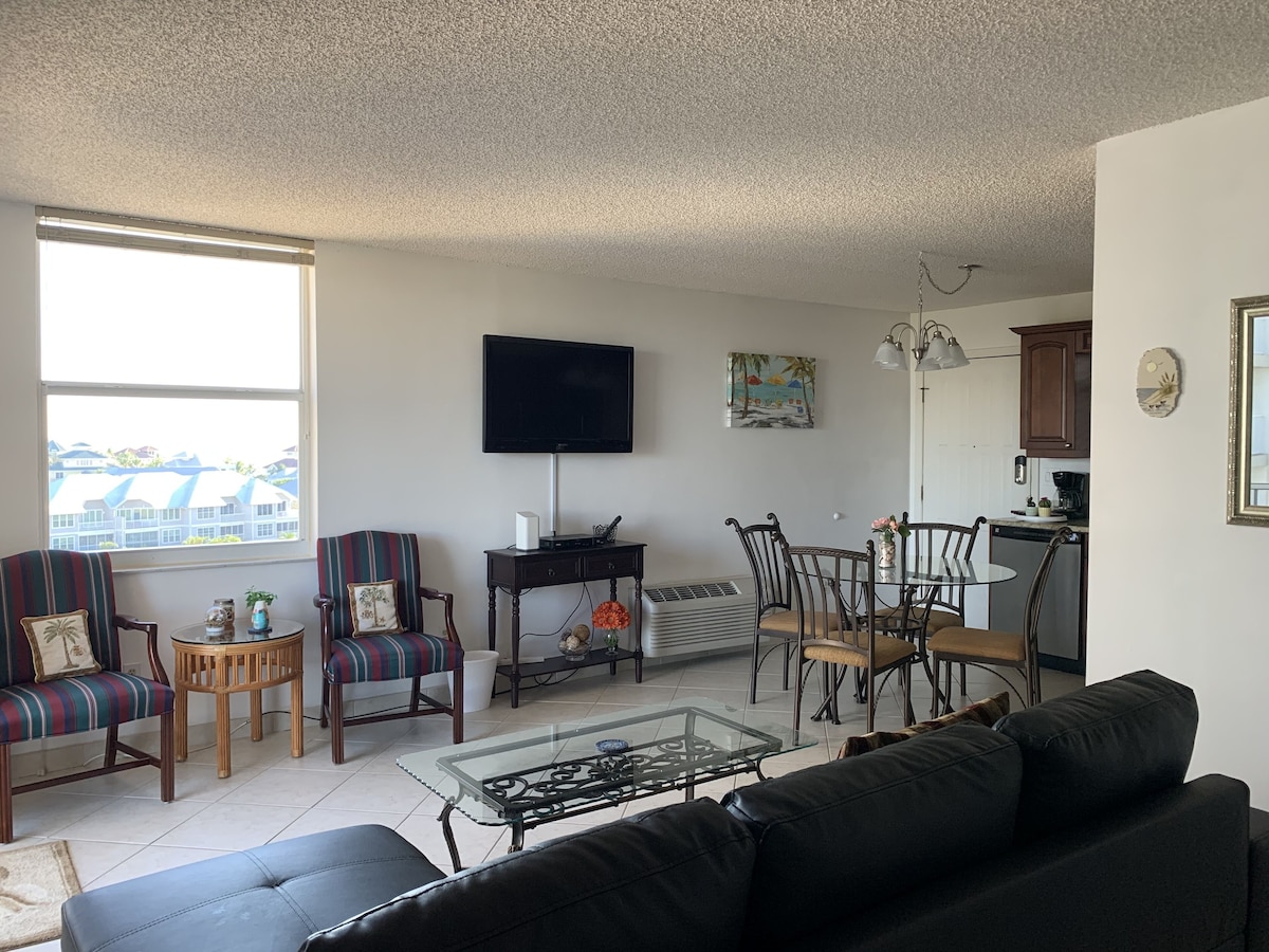 A living room with a sofa, armchairs, a coffee table, a TV, and a dining area with chairs and a table.