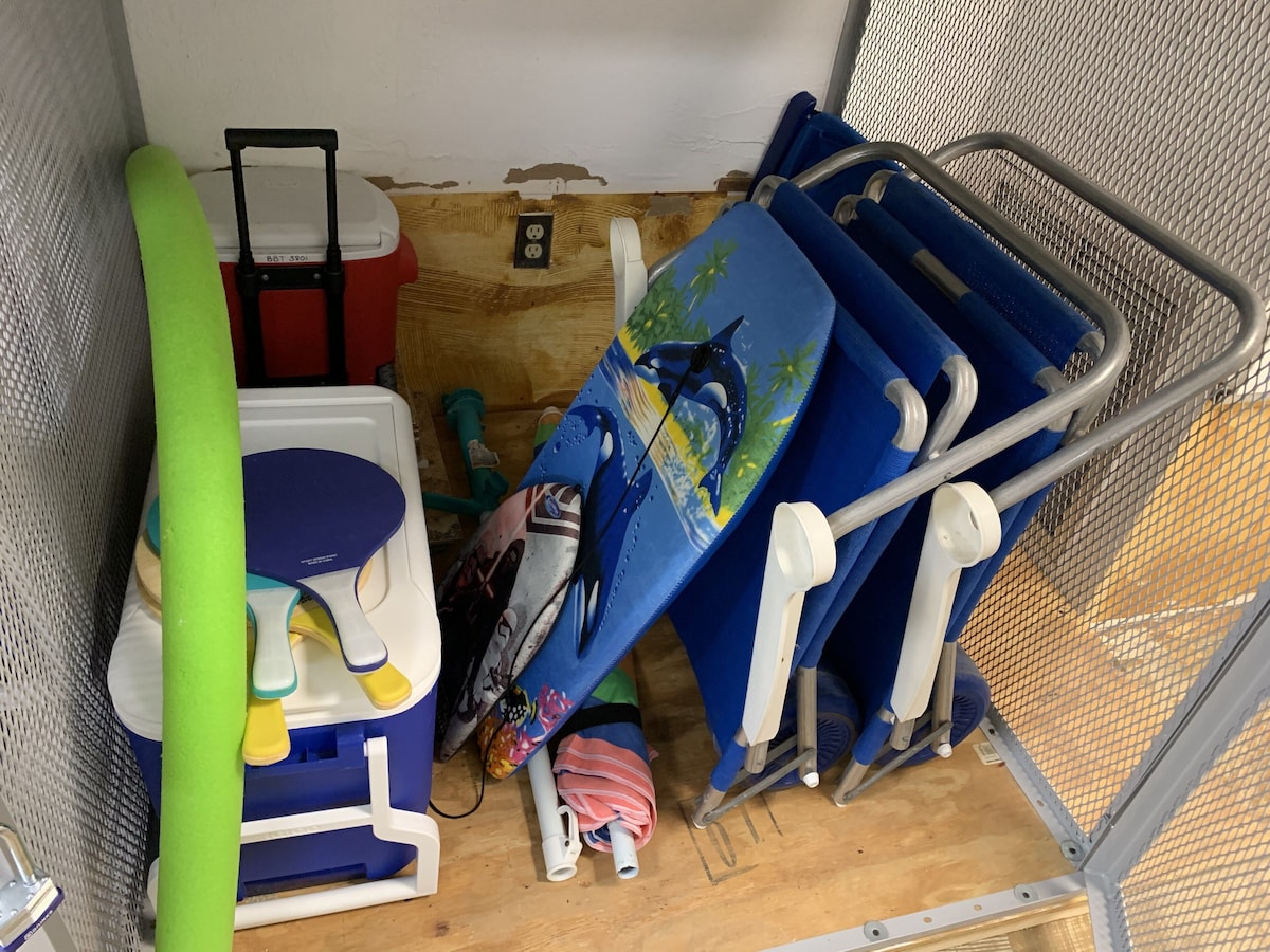 A cluttered storage area with various items including a green mat, a blue folding chair, and a white plastic container.