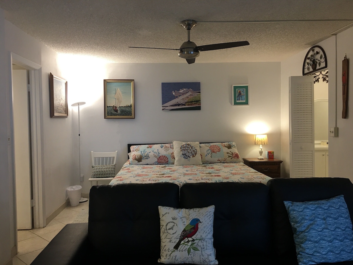 A bedroom with a bed, a ceiling fan, and wall-mounted artwork.