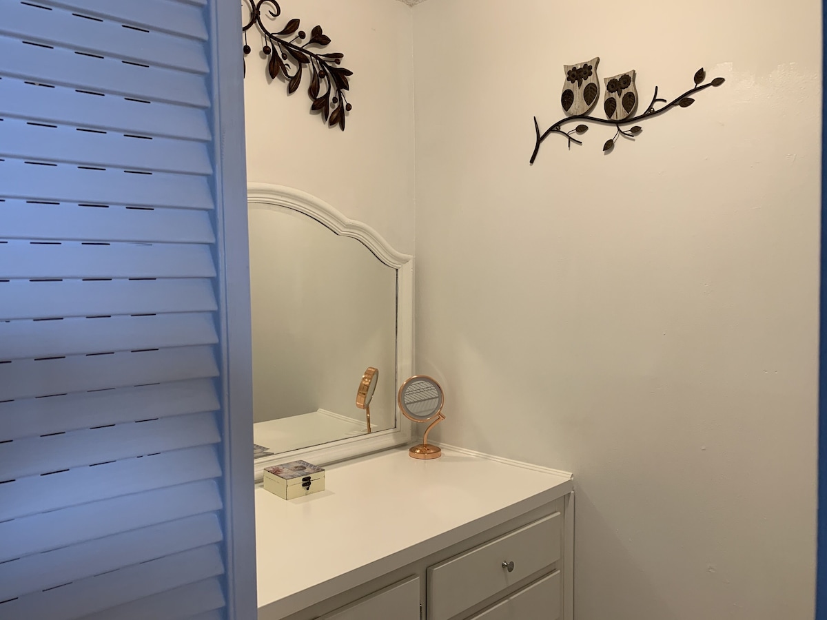A bathroom with a white vanity, a mirror, and decorative wall art.