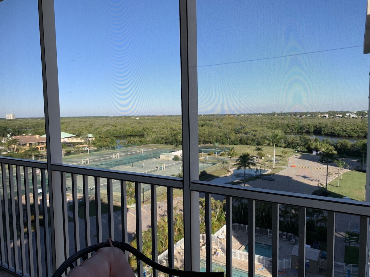 A balcony with a view of a sports court, greenery, and distant buildings.