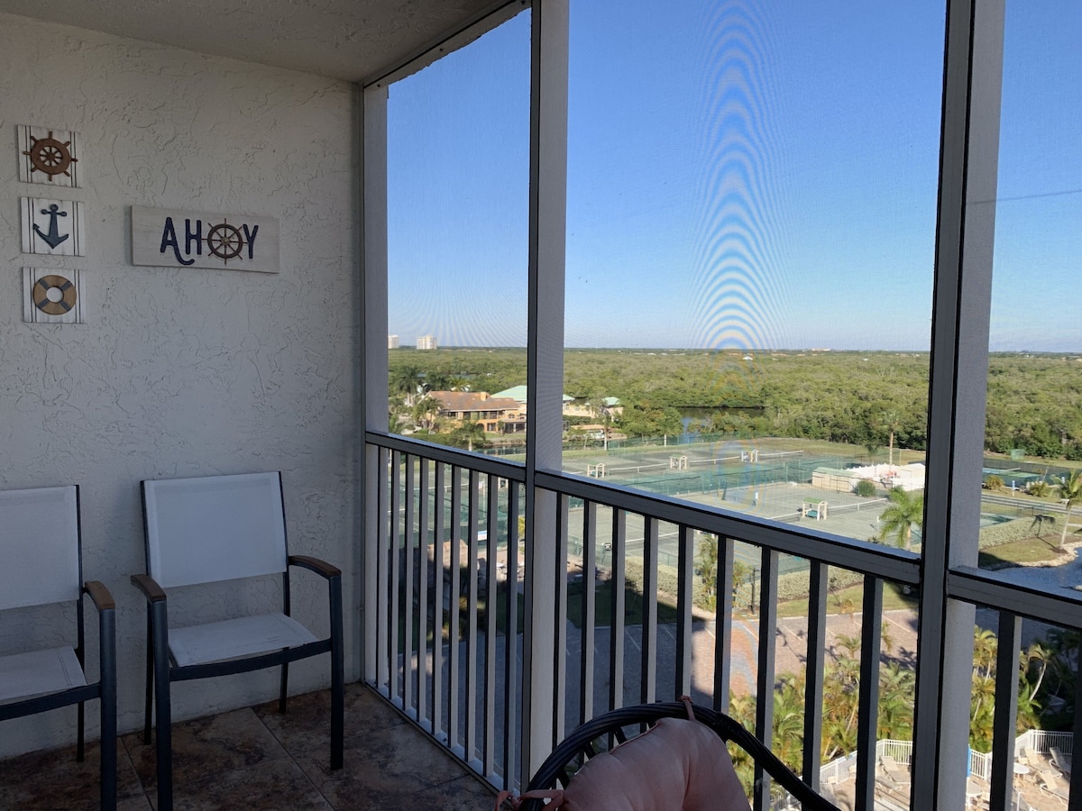 A balcony with two chairs, a view of a green landscape, and a clear sky.