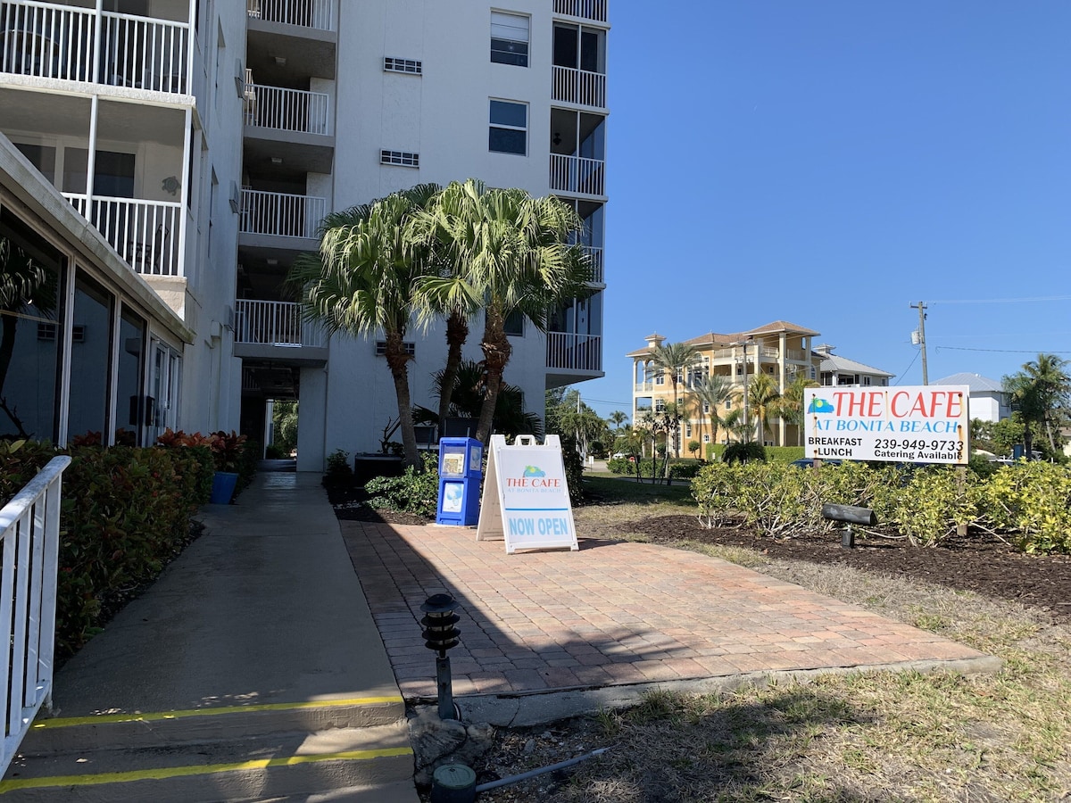 A pathway leading to a building with a sign for The Cafe at Bonita Beach offering breakfast and lunch.