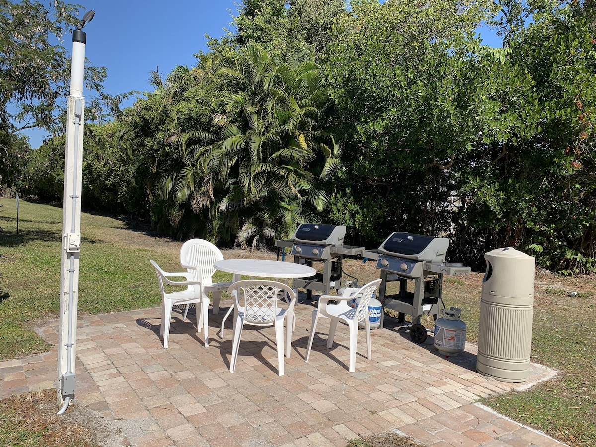 An outdoor patio with a table and chairs, a grill, and a trash can.