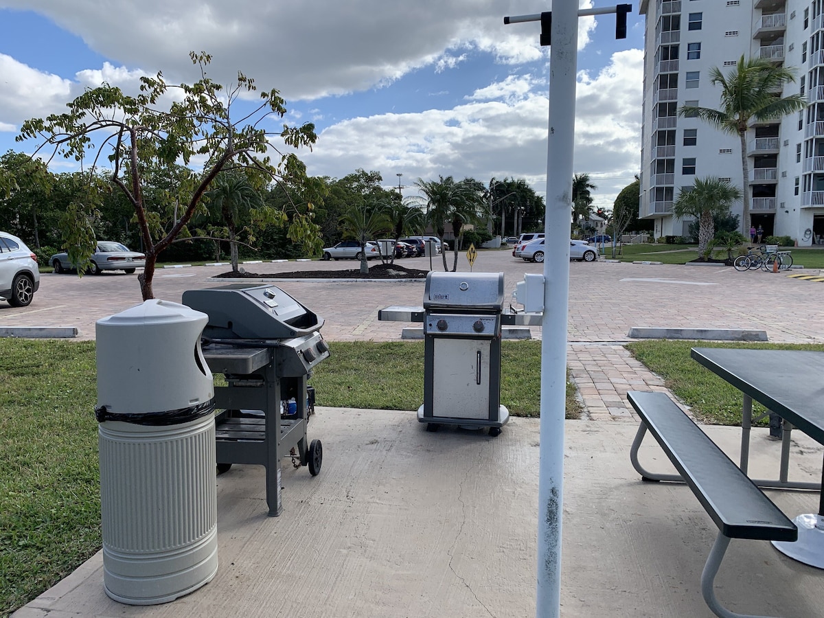 A picnic area with a grill, trash can, and benches.