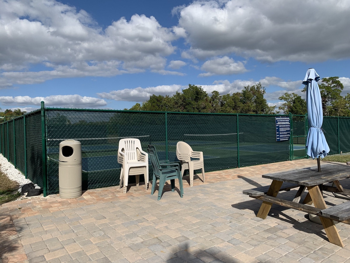 An outdoor seating area with chairs and a table, a trash can, and a fence.