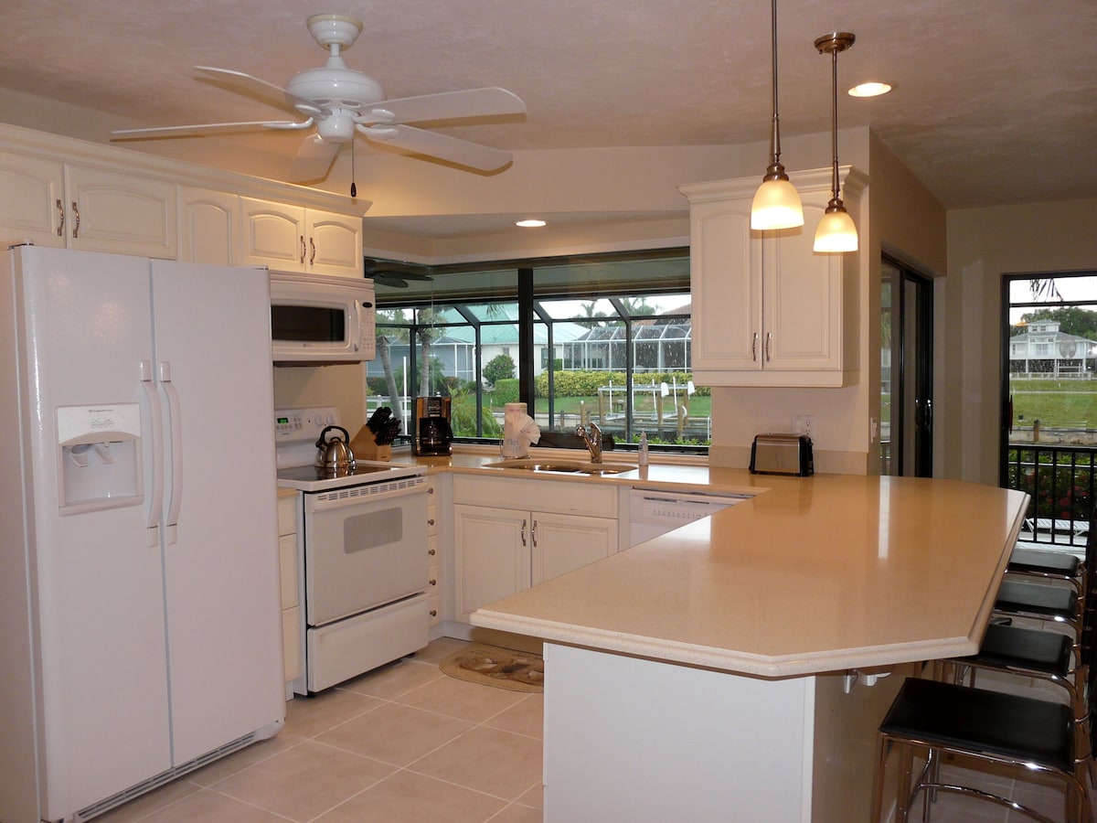 A kitchen with white cabinets, a refrigerator, an oven, a sink, and a large island with bar stools.