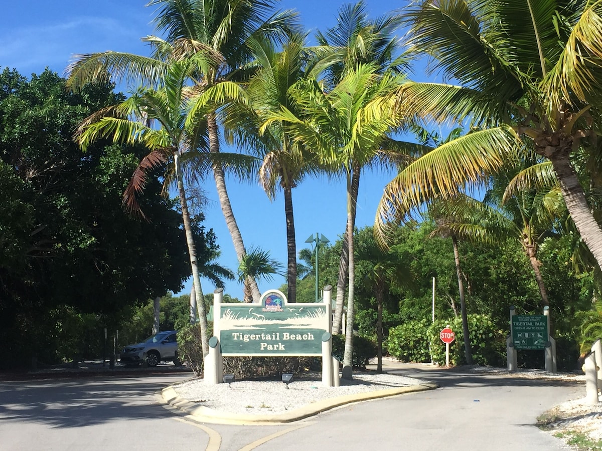 A sign for Tigertail Beach Park with a stop sign nearby.