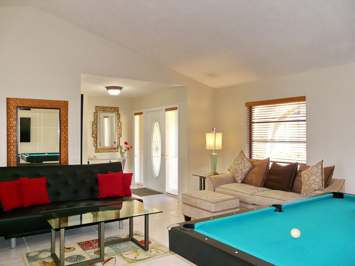 A living room with a pool table, a sofa, a glass coffee table, and a lamp.