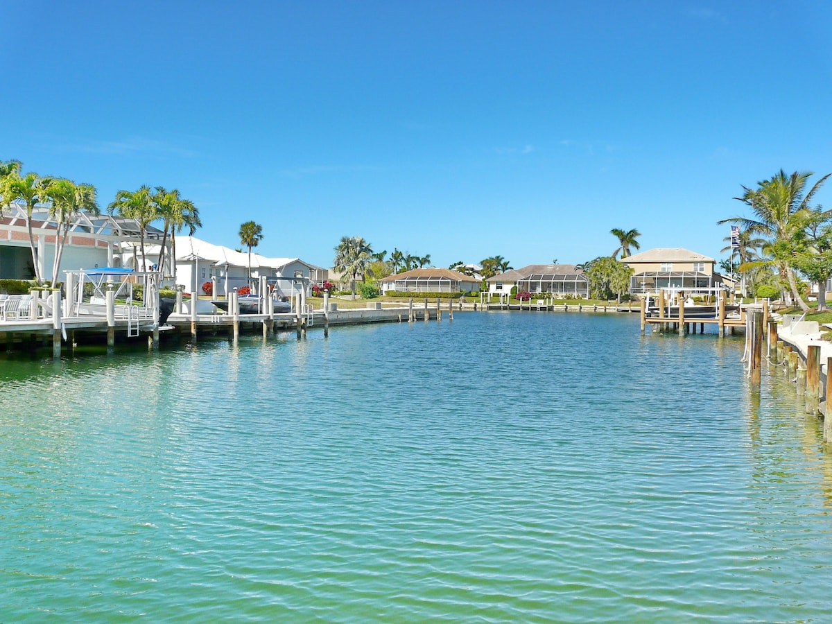 A marina with docked boats, waterfront houses, and palm trees.