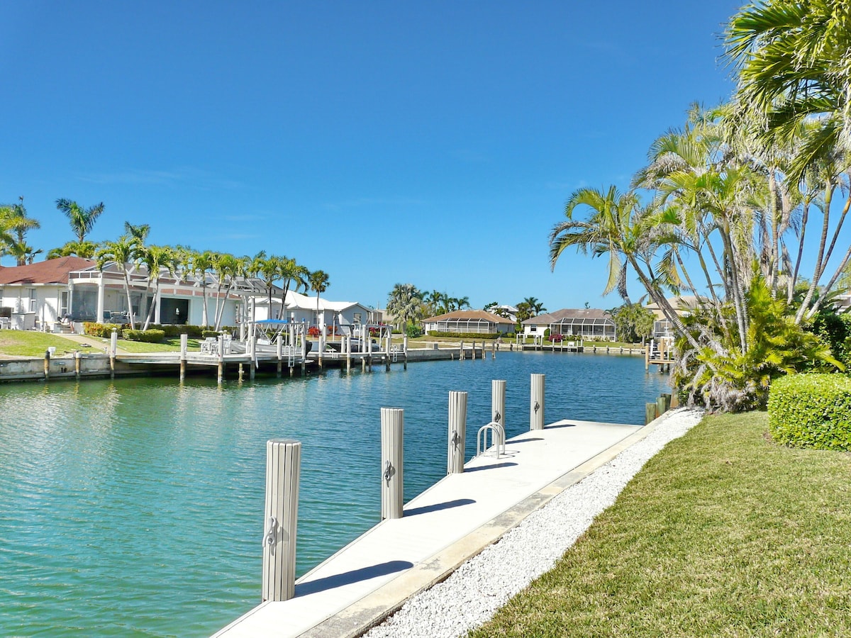 A marina with docked boats, a clear blue sky, and residential buildings with palm trees.