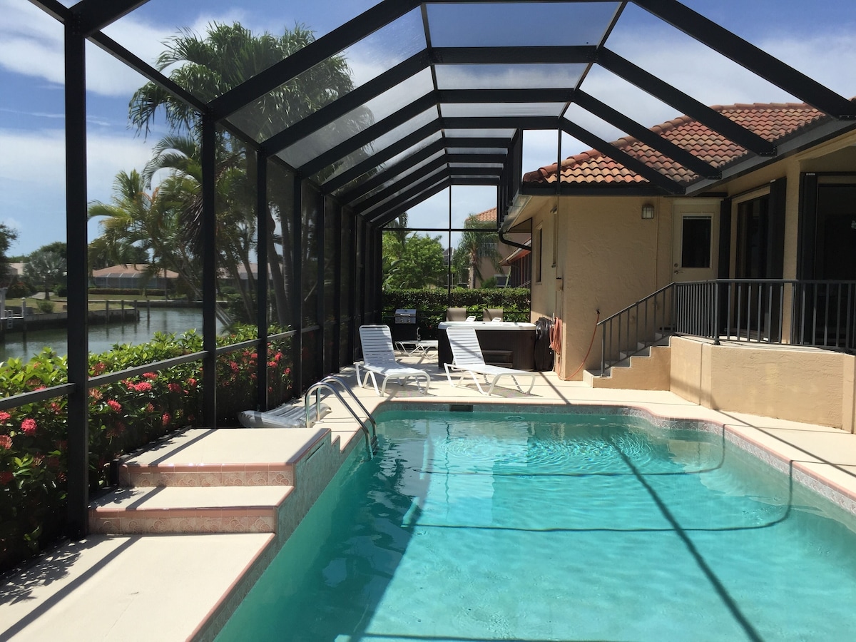 A pool area with a glass-enclosed patio, lounge chairs, and a view of a lake.