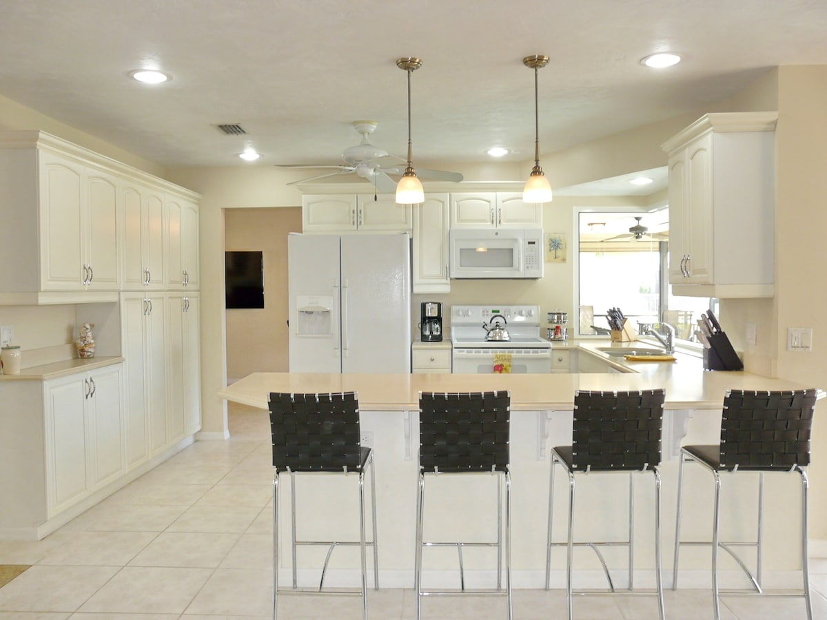 A modern kitchen with white cabinets, a central island with bar stools, a microwave, stove, and a ceiling fan.