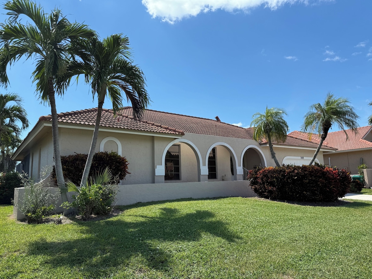 A single-story house with a red-tiled roof, multiple arched windows, and a well-maintained lawn with palm trees.