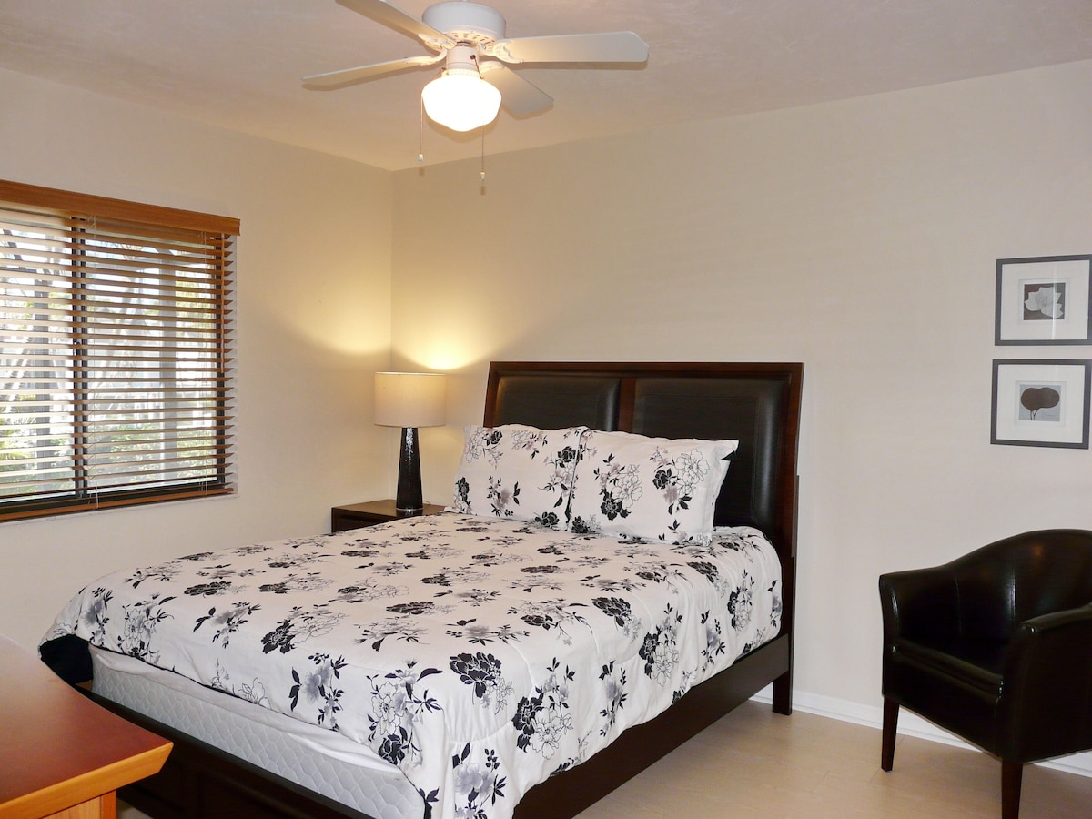 A bedroom with a bed, a nightstand, a lamp, a ceiling fan, and a chair.