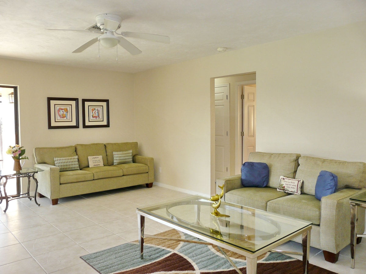A living room with two sofas, a glass coffee table, and a ceiling fan.