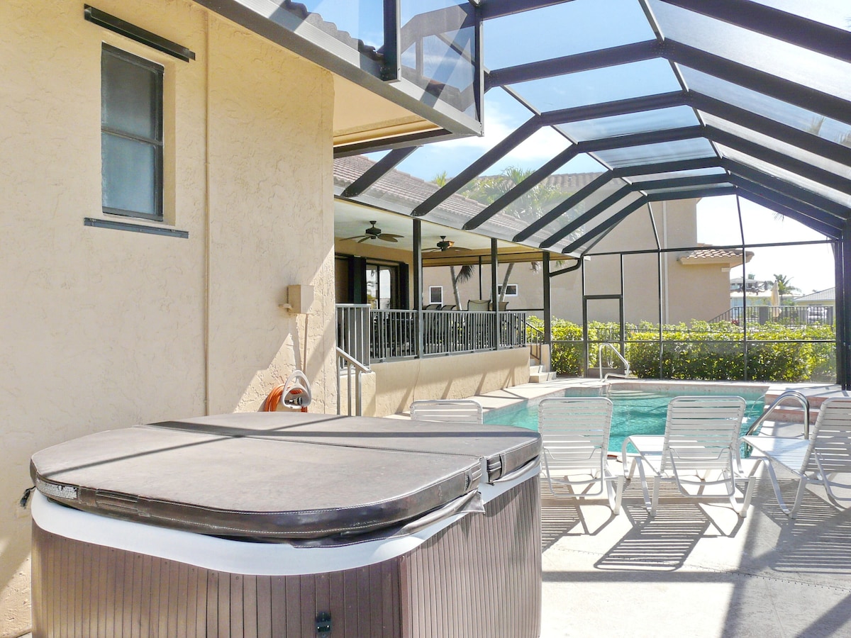A covered outdoor area with a hot tub, lounge chairs, and a pool.