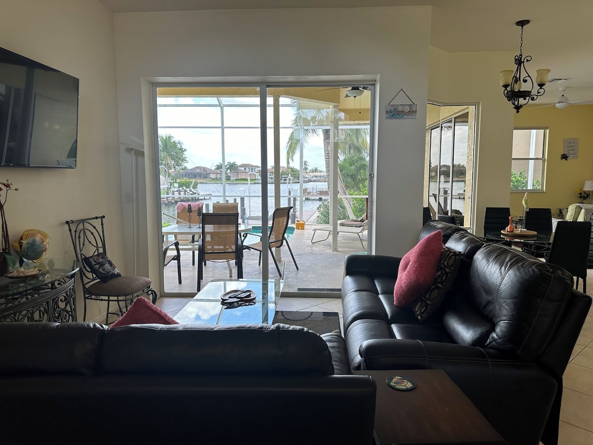 A living room with a black leather sofa, a glass coffee table, and a dining area with chairs and a table.
