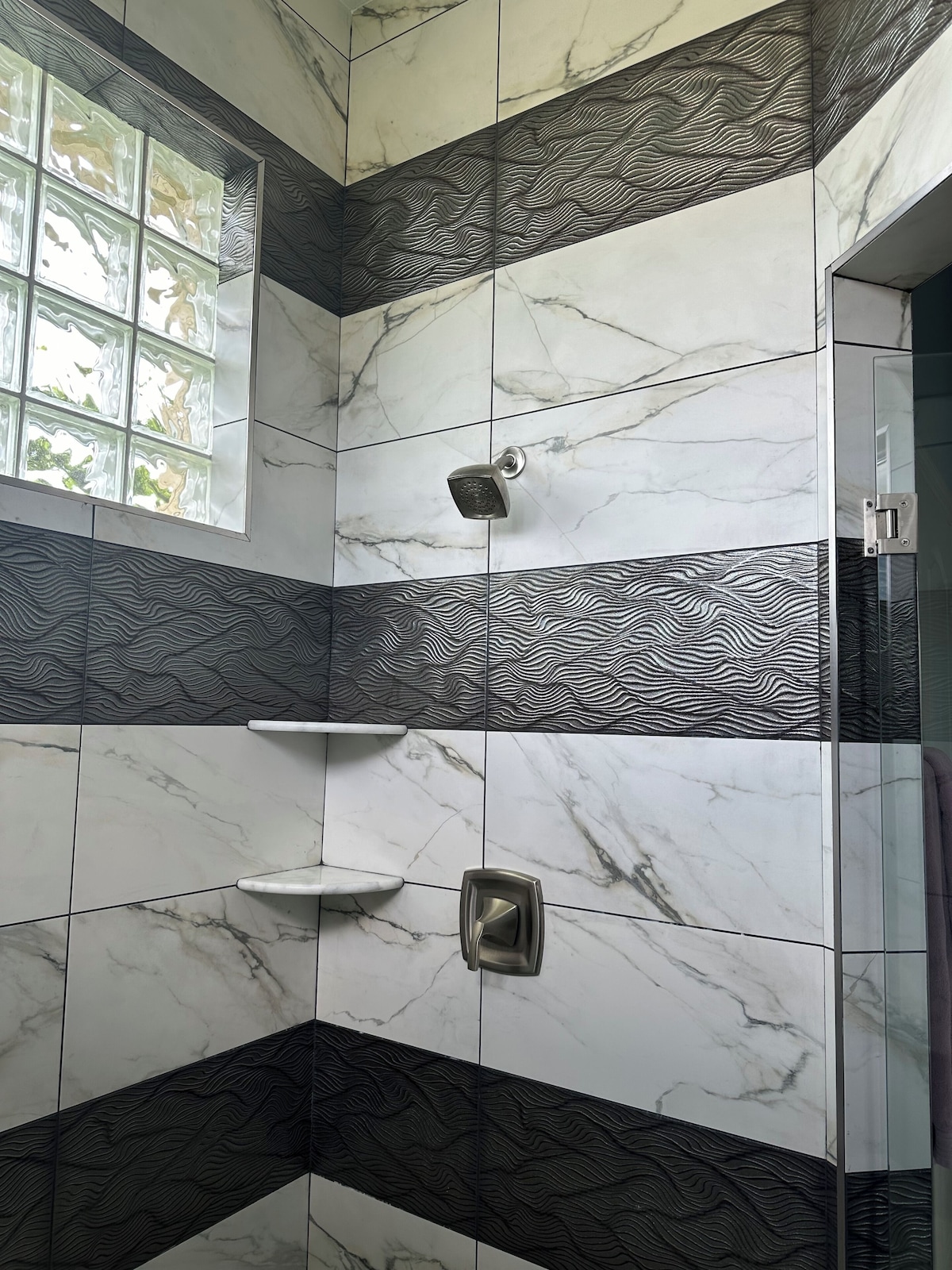 A bathroom with a shower, marble tiles, and a window.