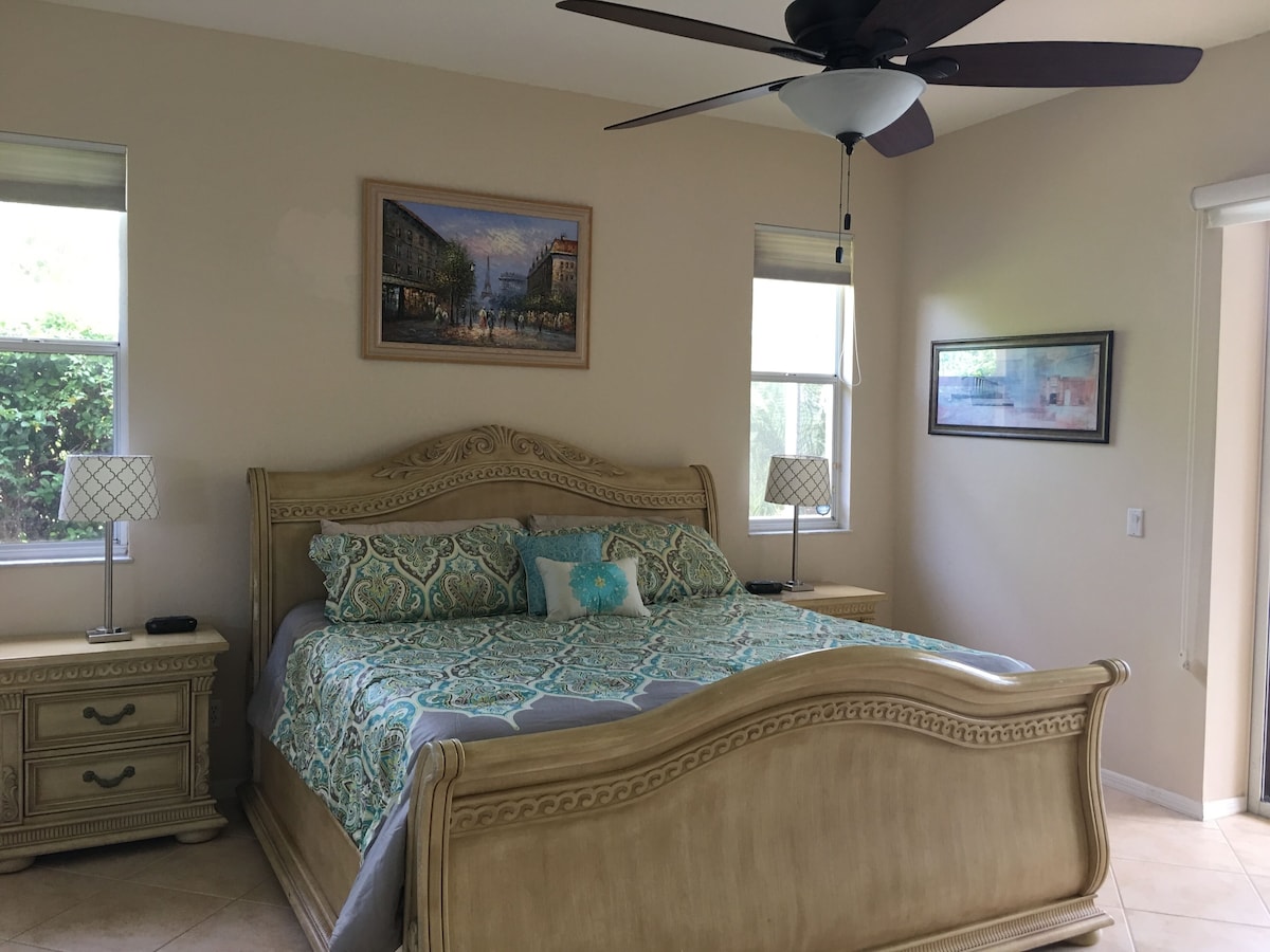 A bedroom with a bed, two bedside tables, a ceiling fan, and two windows.