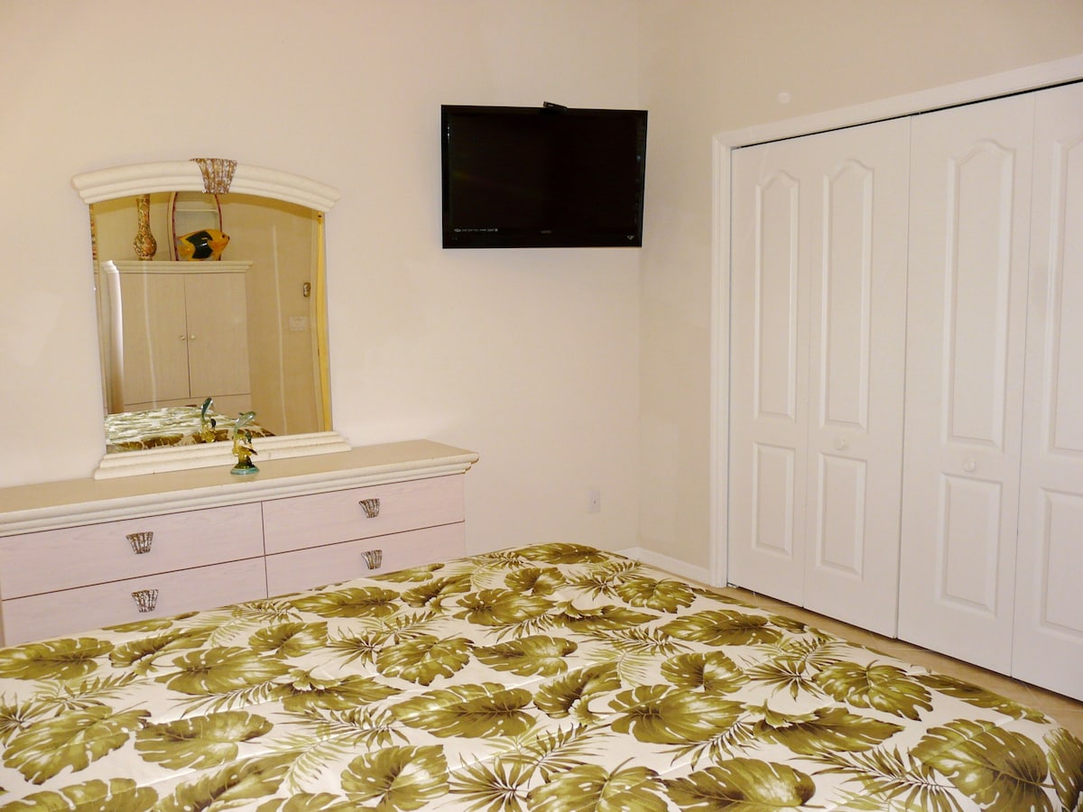 A bedroom with a bed, a dresser, a mirror, a television, and a wardrobe.