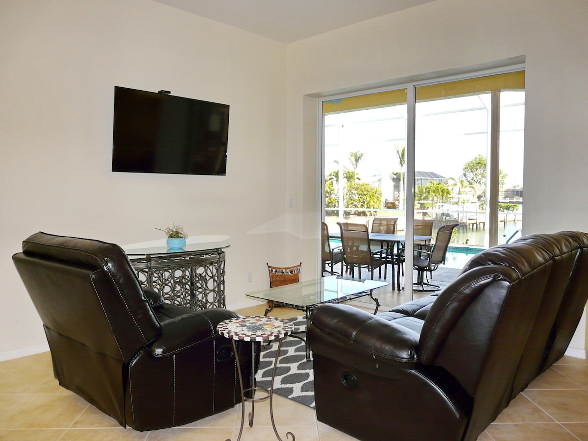 A living room with a sofa, a coffee table, and a TV mounted on the wall.