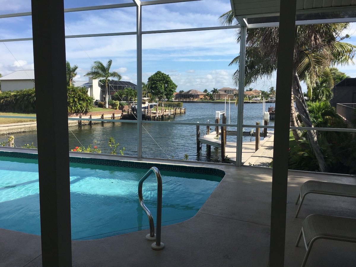 A pool with a metal railing, a view of a marina with boats, and a clear sky.