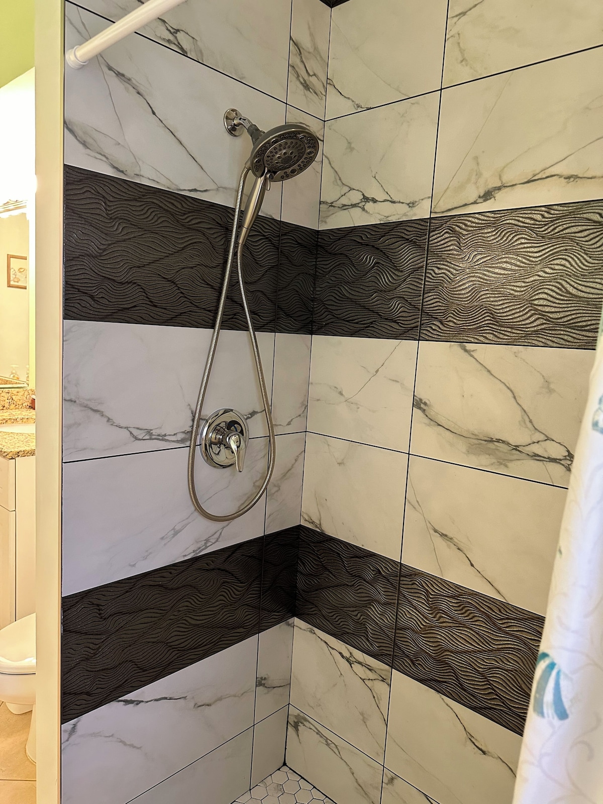 A shower with a handheld showerhead, black and white marble tiles, and a hexagonal tile pattern on the floor.