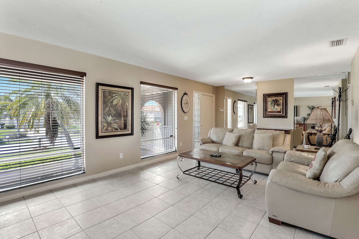 A spacious living room with a beige sofa set, a coffee table, and large windows with blinds.