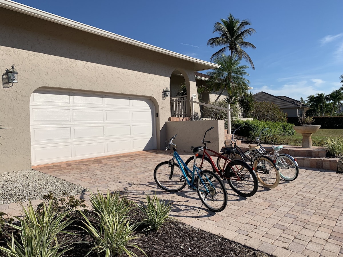 A residential garage with a white garage door, a brick driveway, and several bicycles parked outside.
