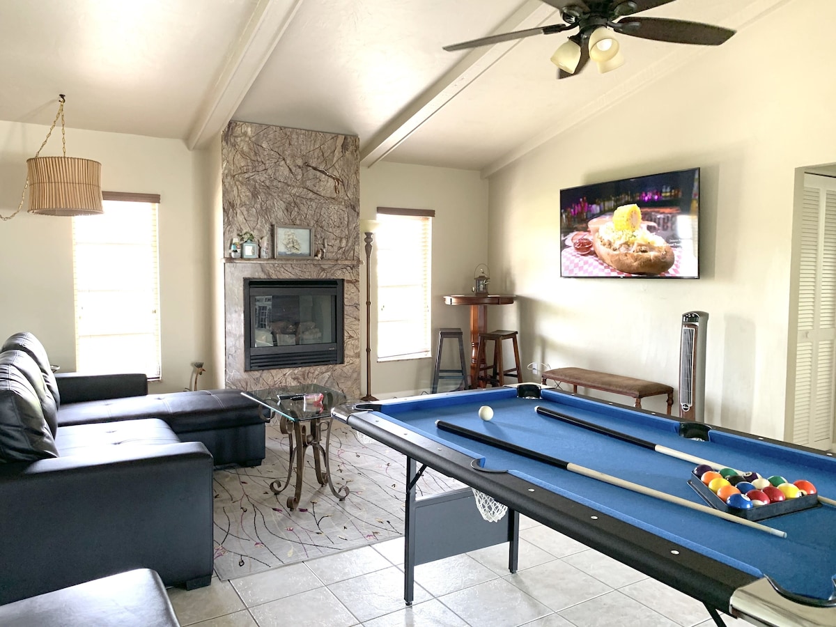 A living room with a pool table, a sofa, a fireplace, and a television.