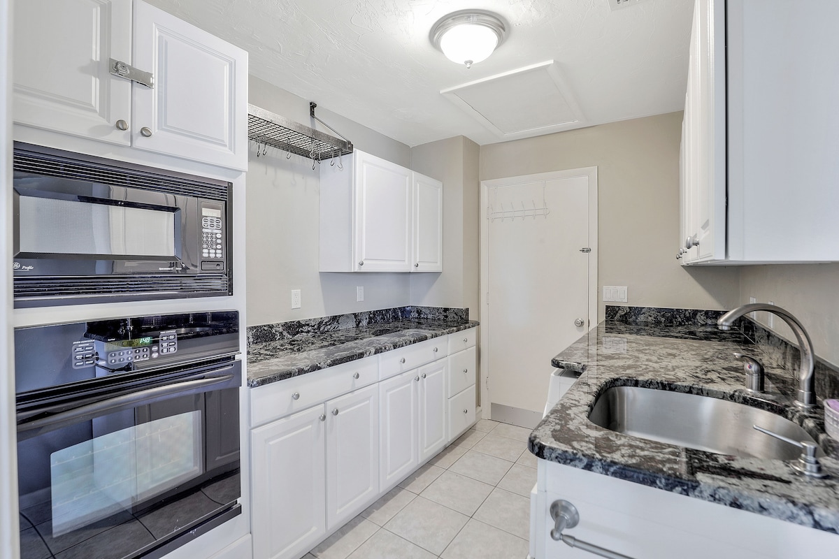 A kitchen with white cabinets, a stainless steel sink, and a black microwave.